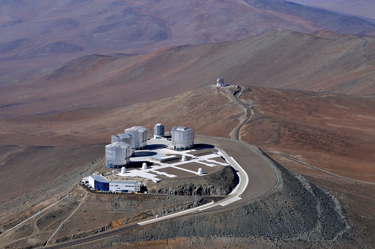 The Very Large Telescope. White buildings surrounded by mountainous desert. Another smaller building can be seen in the background.