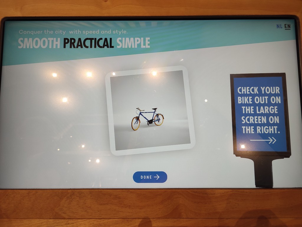 On a tablet screen, a bike sits in the centre within a polaroid-like frame. At the top left, the words "Smooth, Practical, Simple" appear. The right side of the screen says "Check your bike out on the large screen to the right."